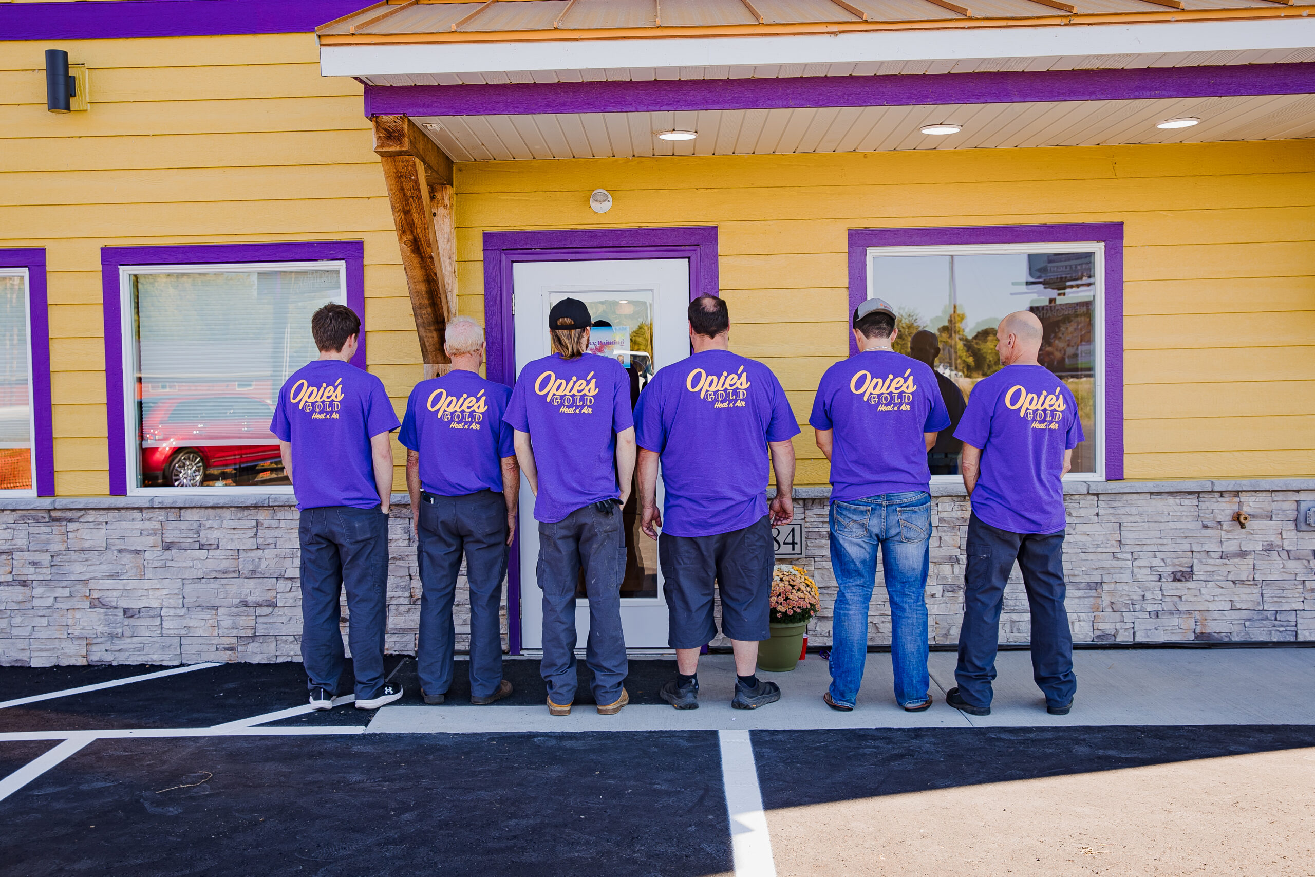 Five people in purple shirts stand facing away from the camera outside a building painted yellow and purple.