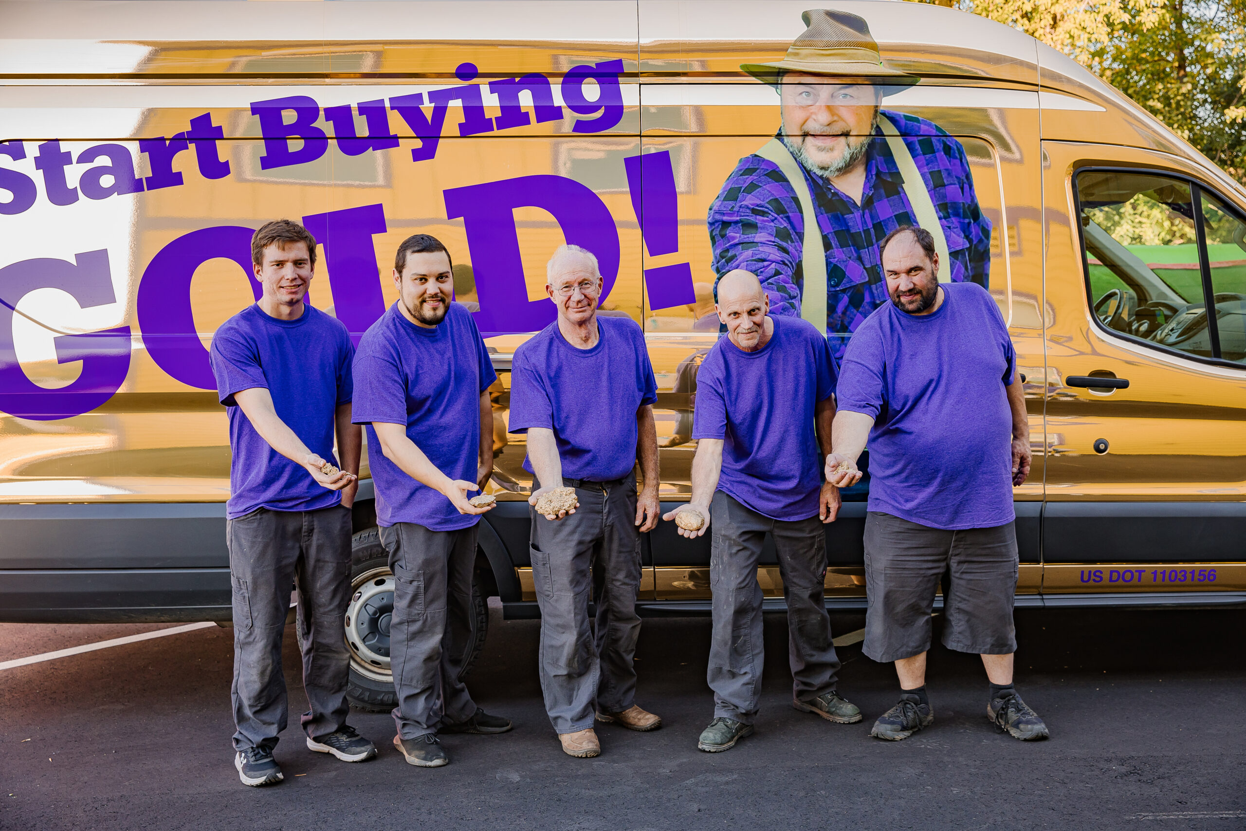 Five men wearing purple shirts stand in front of a van that displays the slogan "Start Buying Gold!
