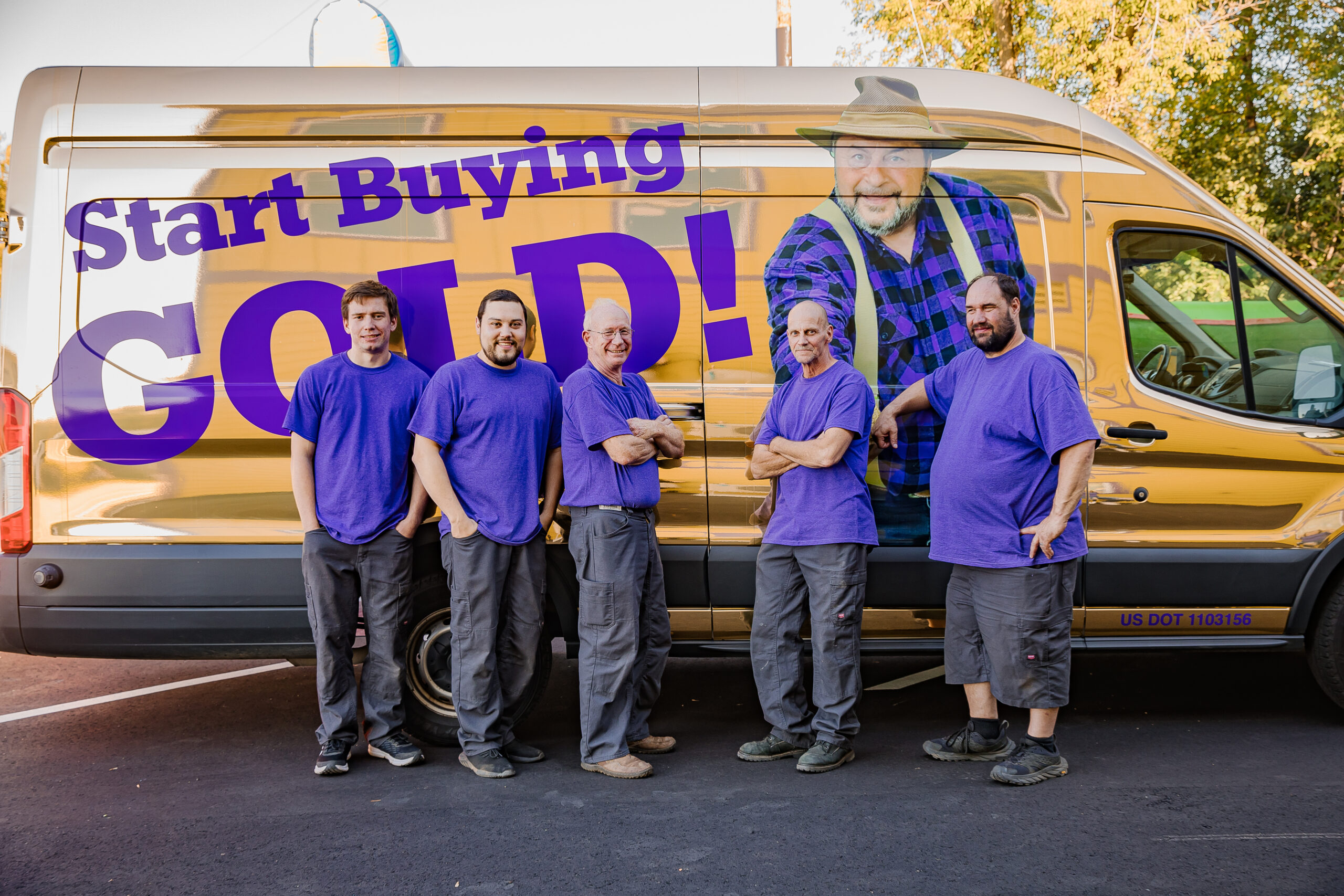 Five men wearing purple shirts stand in front of a gold van displaying the message "Start Buying Gold!
